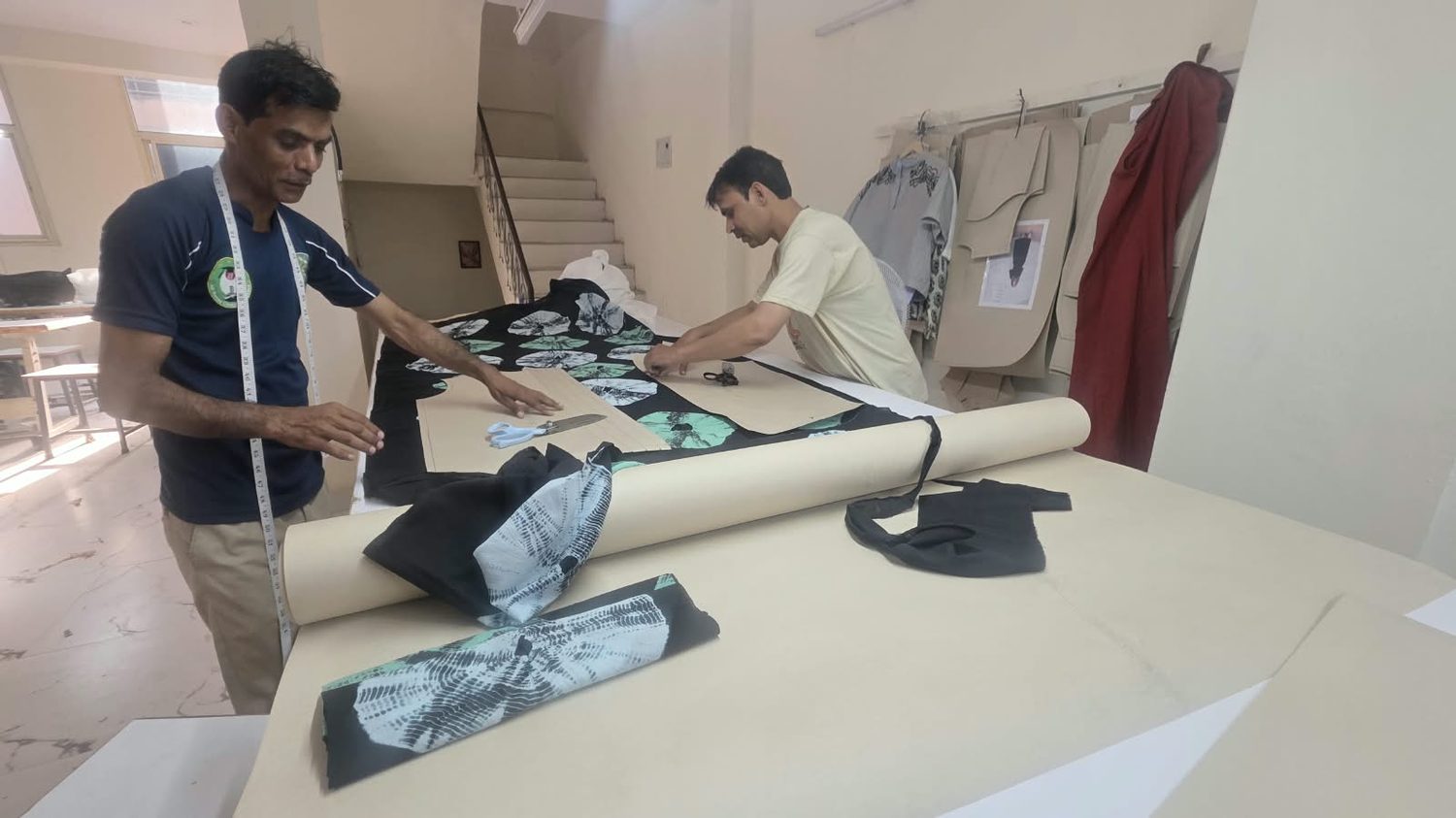 Two cutters laying pattern pieces over printed fabric on the cutting table.