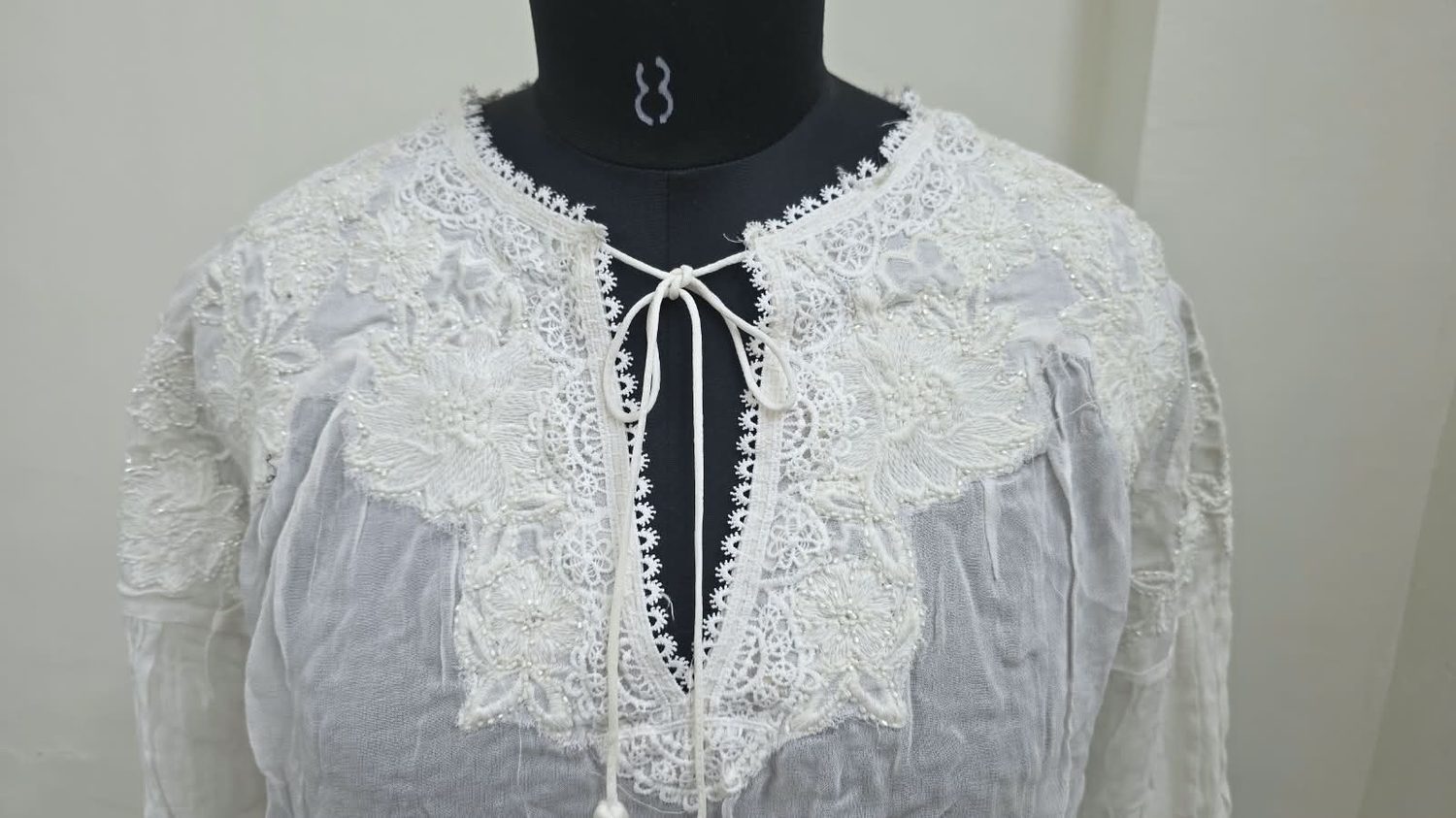 Close view of a lace and bead-worked yoke on a sheer cotton blouse.