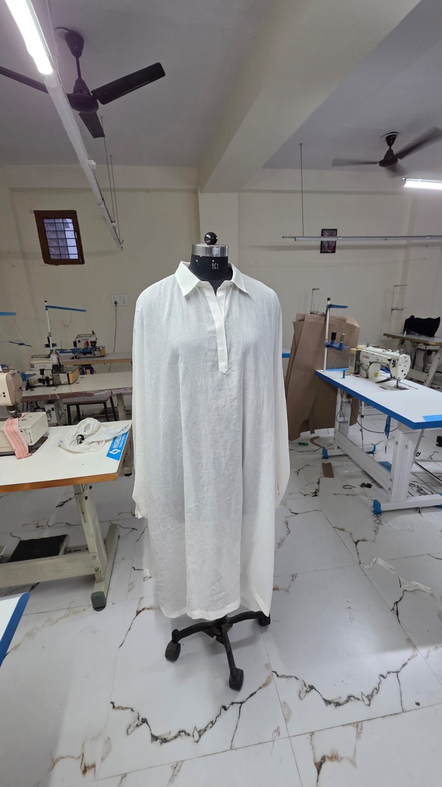 A white linen shirt dress on a dress form in the sampling room.