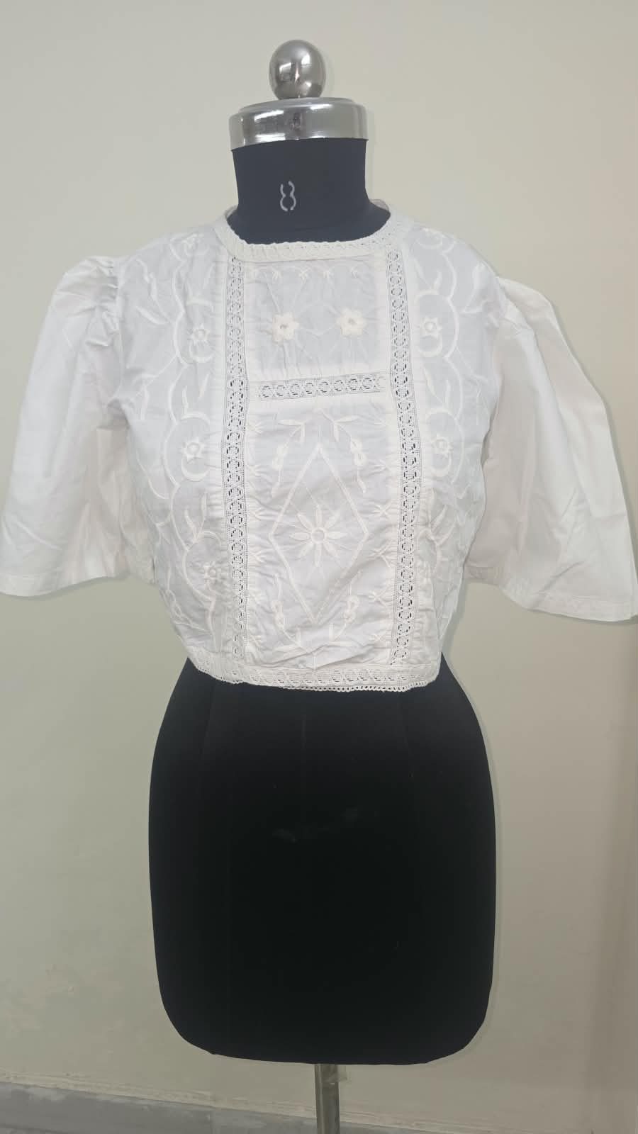 A white cotton crop blouse with whitework embroidery and lace insertion down the centre panel.